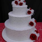 White 3-Tiered Cake is covered in white satin with embroidered leaves. White pearls circle the base of each tier. Chiffon & pearl trim circle the top of each tier. Red roses adorn each tier. Very elegant for large weddings. Roses can be in your wedding color.